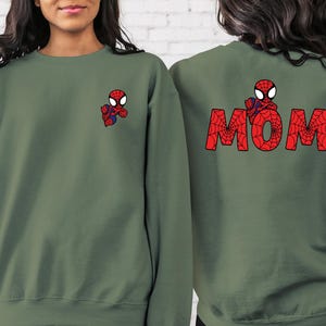 May include: Two green sweatshirts with a red and black Spiderman design. One sweatshirt has the word "MOM" spelled out in red and black Spiderman design.