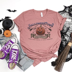 May include: A pink t-shirt with a graphic design of a pumpkin with a spooky face. The text on the shirt reads "Halloweentown University est. 1996" and "Where being normal is vastly overrated".