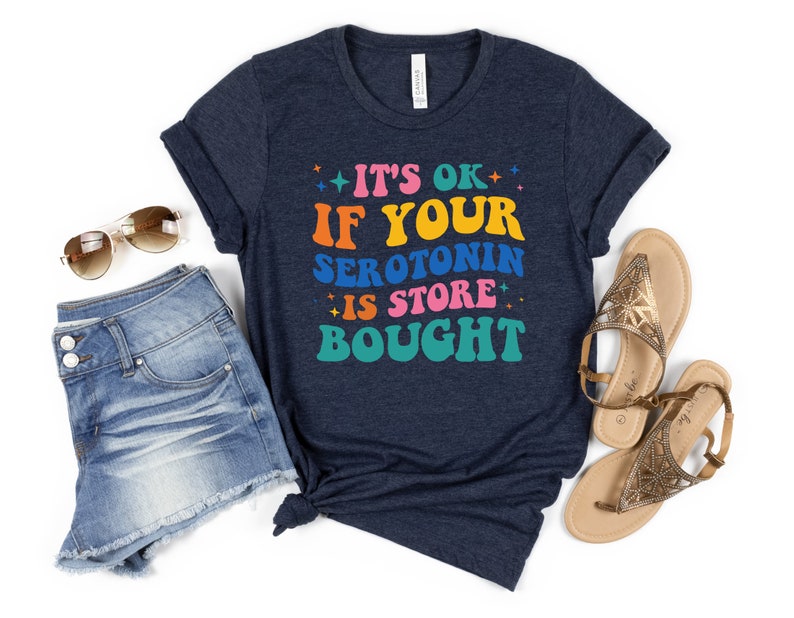 Puede incluir: Una camiseta azul marino con un gr&aacute;fico colorido que dice "Est&aacute; bien si tu serotonina se compra en la tienda".