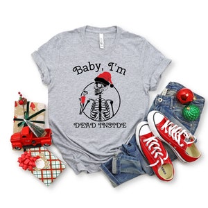May include: A gray t-shirt with a skeleton wearing a Santa hat and holding a drink. The text on the shirt reads "Baby, I'm Dead Inside".