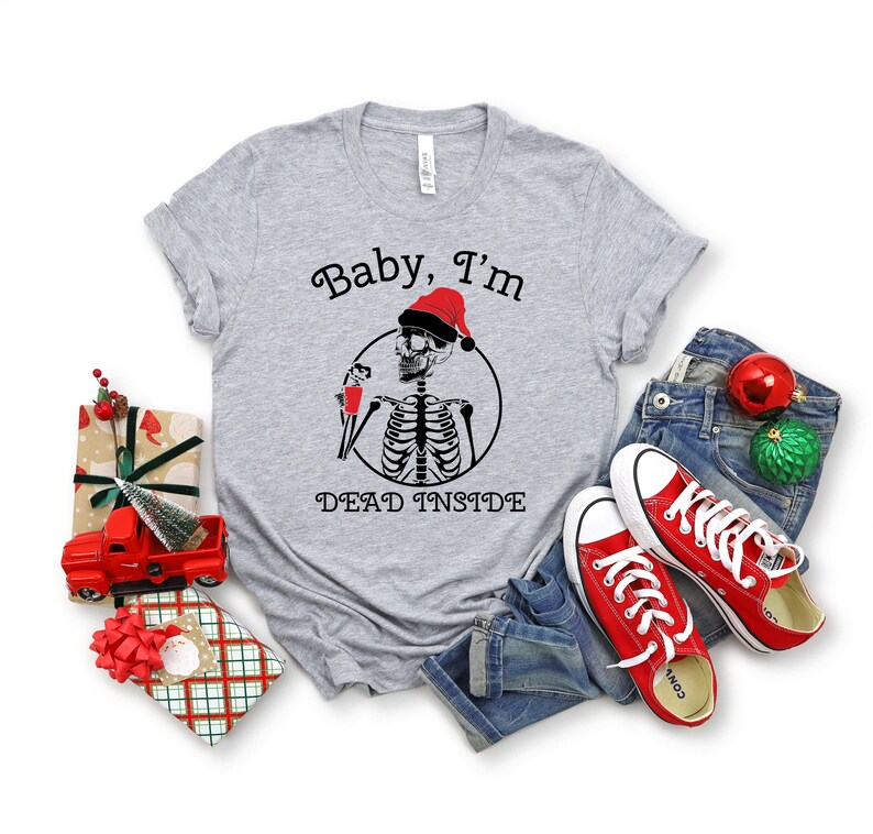 May include: A gray t-shirt with a skeleton wearing a Santa hat and holding a drink. The text on the shirt reads "Baby, I'm Dead Inside".