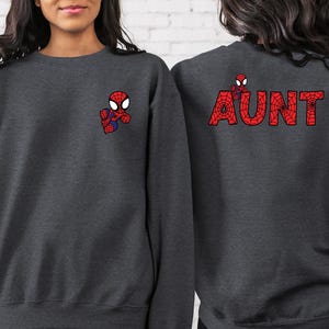 May include: Two dark grey sweatshirts with a Spiderman graphic. One sweatshirt has a small Spiderman graphic on the front and the other has the word "AUNT" spelled out in red with a Spiderman graphic in each letter on the back.