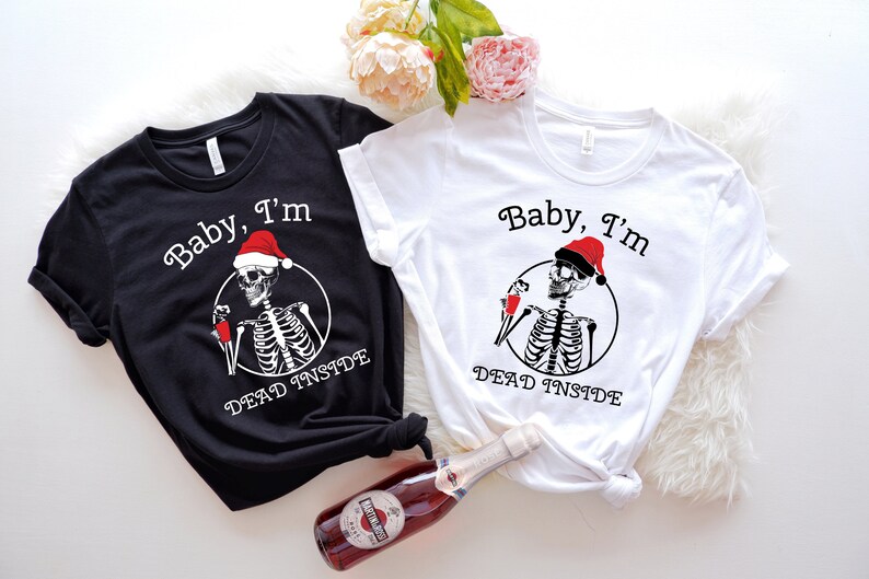 May include: Two black and white t-shirts with a skeleton wearing a Santa hat and holding a glass of wine. The text on the shirts reads "Baby, I'm Dead Inside".