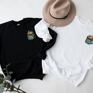 May include: Two sweatshirts, one black and one white, with a graphic of a green mug filled with Christmas treats and the text "Merry Christmas".