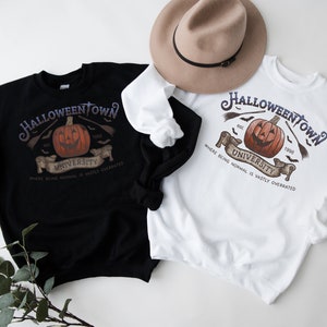 May include: Two sweatshirts with a Halloween Town University graphic. The graphic features a jack-o-lantern with a toothy grin, bats, and the text "Halloween Town University" with the years "est. 1990" and "1996". The sweatshirts are black and white.