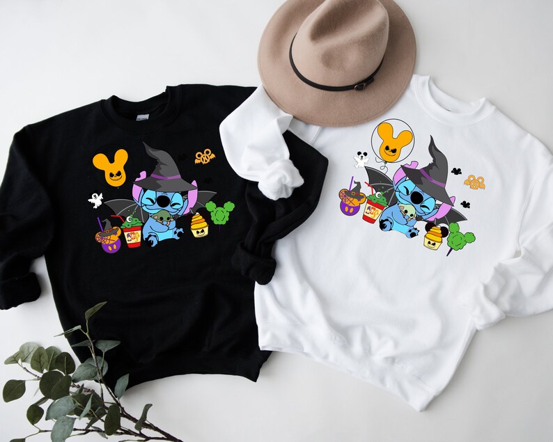 May include: Two sweatshirts featuring a blue Stitch character dressed as a witch holding a green alien. The Stitch character is surrounded by Halloween themed treats and decorations. One sweatshirt is black and the other is white.