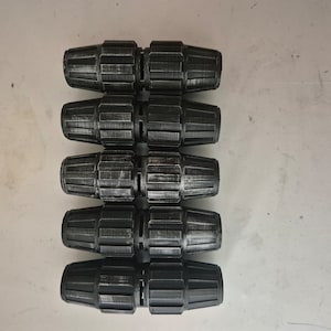 Könnte beinhalten: Fünf schwarze Kunststoff-Rohrverbinder, die übereinander gestapelt sind. Die Verbinder haben ein geriffeltes Design und werden zum Verbinden von Rohren verwendet.