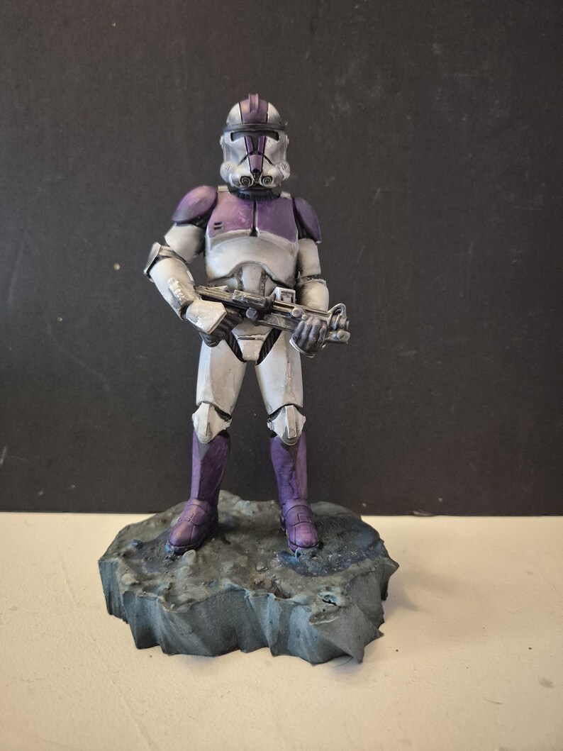 Pu&ograve; includere: Statuetta dettagliata di un soldato con armatura bianca e viola, che tiene un fucile blaster. La figura &egrave; su una base rocciosa grigia. L'elmo e l'armatura sono riccamente dettagliati.