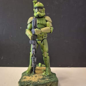 Pu&ograve; includere: Una statuetta d'azione verde e beige di un soldato in armatura, che tiene un fucile nero. La statuetta &egrave; su una base verde con dettagli beige. L'elmetto e l'armatura del soldato sono dettagliati con accenti neri.