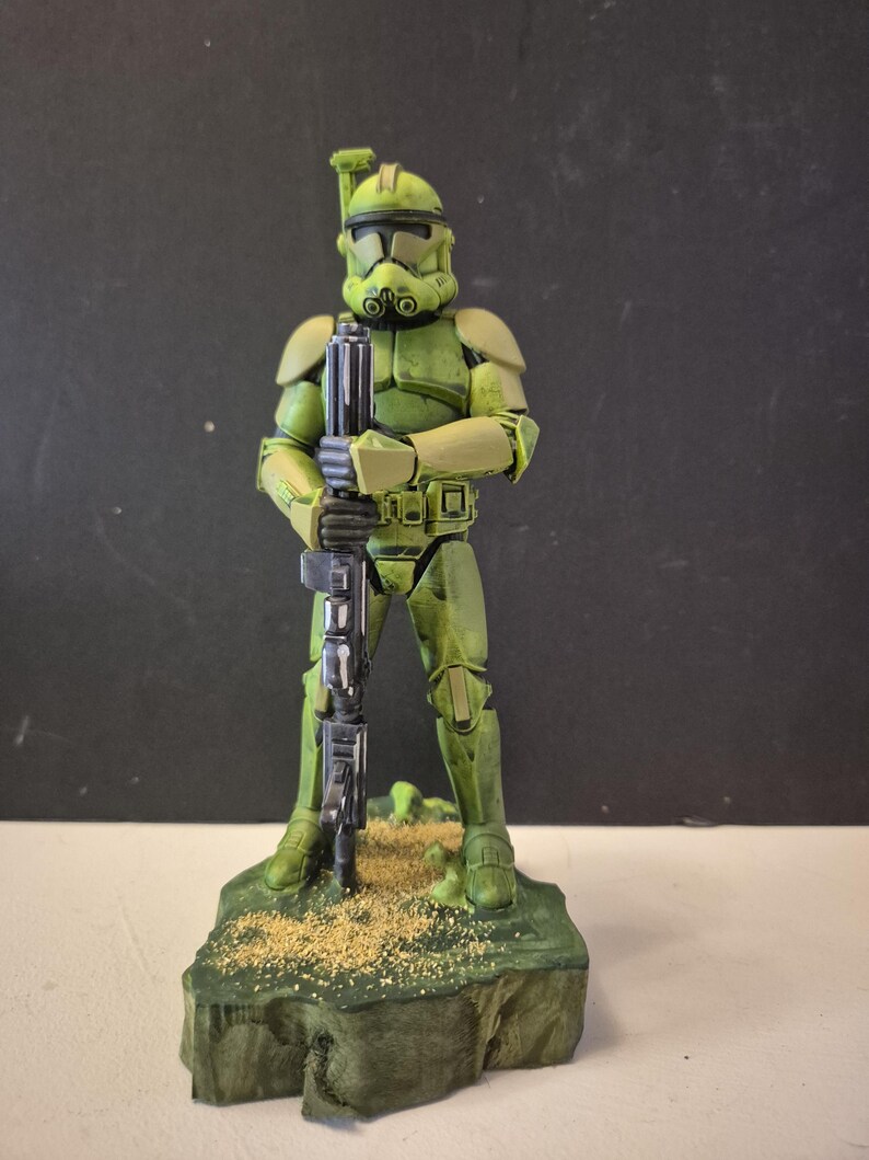 Pu&ograve; includere: Una statuetta d'azione verde e beige di un soldato in armatura, che tiene un fucile nero. La statuetta &egrave; su una base verde con dettagli beige. L'elmetto e l'armatura del soldato sono dettagliati con accenti neri.