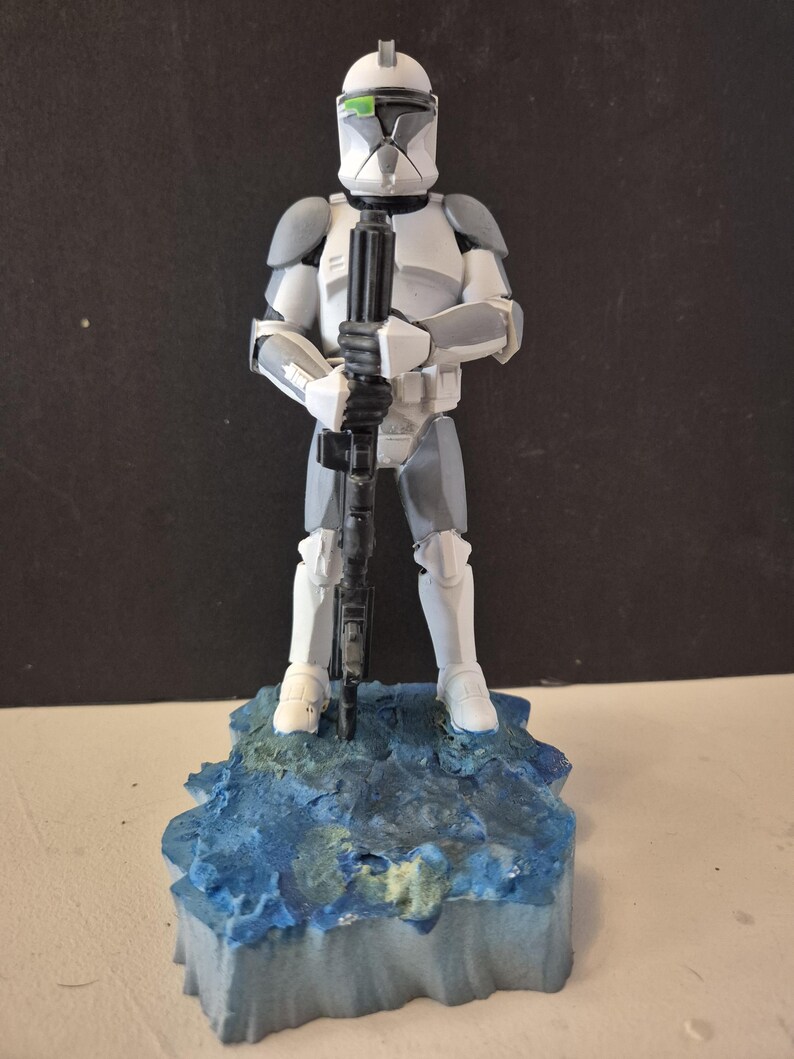 Pu&ograve; includere: Statuetta dettagliata di un soldato corazzato bianco e grigio che tiene un fucile nero. La figura &egrave; su una base strutturata blu e verde. Il casco ha una visiera verde. &Egrave; un oggetto da collezione.