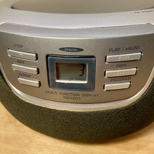May include: A silver portable CD player with a digital display showing the number 3. The device has buttons for stop, rewind, repeat, play/pause, forward, and program. The text "MULTI FUNCTION DISPLAY PD5201" is printed below the display.