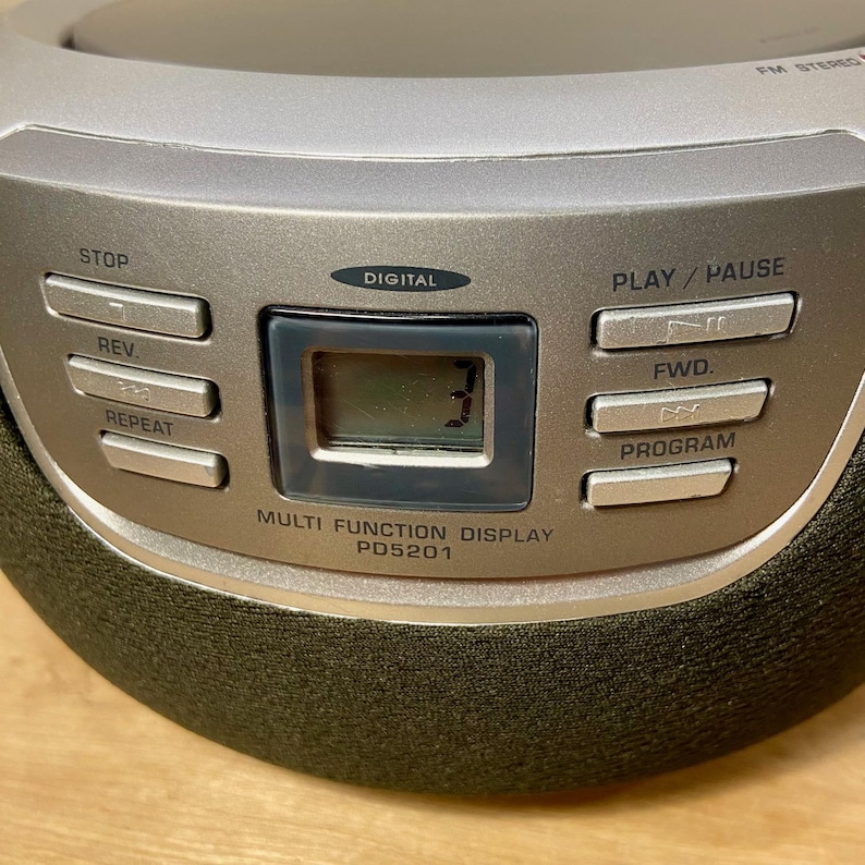May include: A silver portable CD player with a digital display showing the number 3. The device has buttons for stop, rewind, repeat, play/pause, forward, and program. The text "MULTI FUNCTION DISPLAY PD5201" is printed below the display.