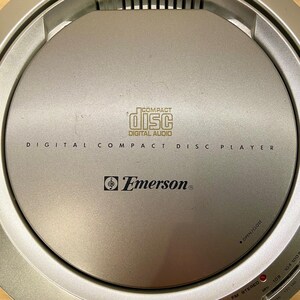 May include: Silver Emerson digital compact disc player. The player has the words "COMPACT DISC DIGITAL AUDIO" printed on the top. The player also has the Emerson logo and the words "DIGITAL COMPACT DISC PLAYER" printed on the top.