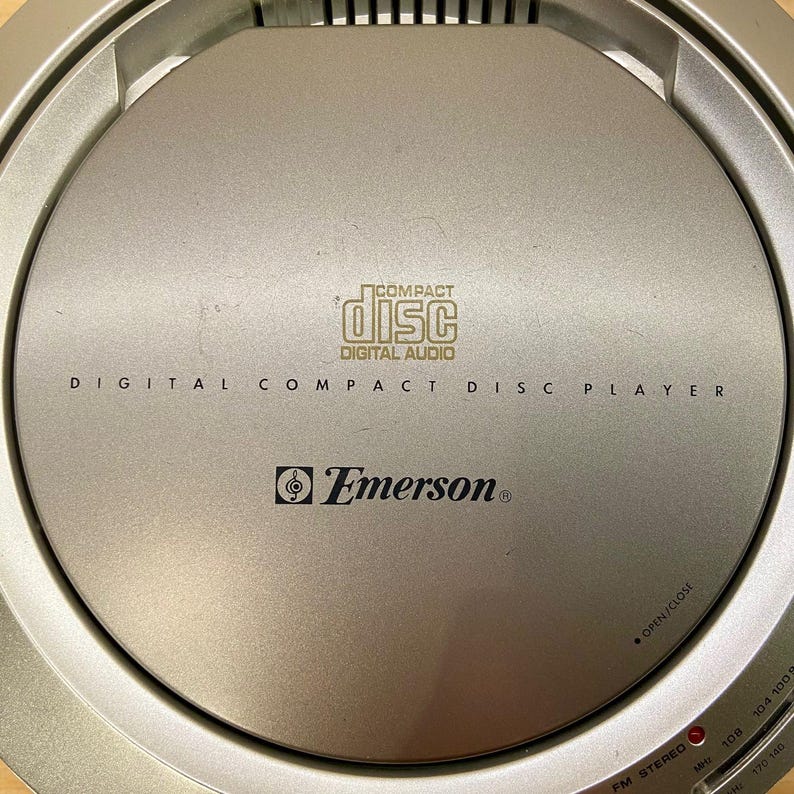 May include: Silver Emerson digital compact disc player. The player has the words "COMPACT DISC DIGITAL AUDIO" printed on the top. The player also has the Emerson logo and the words "DIGITAL COMPACT DISC PLAYER" printed on the top.