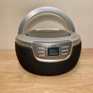 May include: A silver and black portable CD player with a handle. The player has a digital display and control buttons for stop, rewind, repeat, play/pause, and forward. The model number is PD5201.