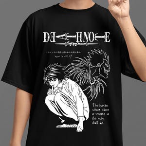Könnte beinhalten: Schwarzes T-Shirt mit einem weißen Death Note Anime-Motiv. Das Design enthält japanischen Text, Charakterillustrationen und englischen Text: "The human whose name is written in this note shall die."