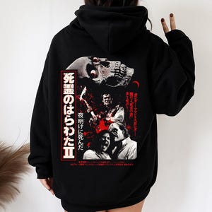 May include: Black hoodie featuring a graphic design with a skull, a man playing a guitar, and screaming faces. Japanese text is also present. The design is in red and white, set against a black background.