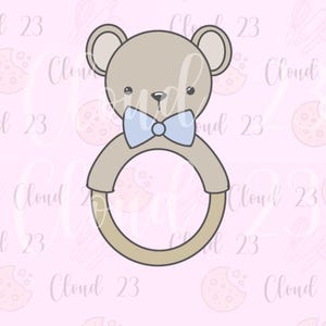 May include: A light brown teddy bear cookie cutter with a blue bow tie and a circular handle. The design is on a pink background with the text "Cloud 23" repeated throughout.