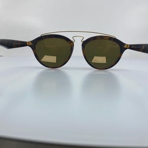 May include: Tortoise shell sunglasses with gold accents and brown lenses. The sunglasses have a thin metal bridge and a wire frame.