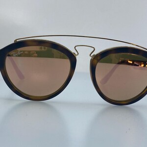 May include: Tortoise shell frame sunglasses with gold accents and mirrored lenses. The lenses are a rose gold color.