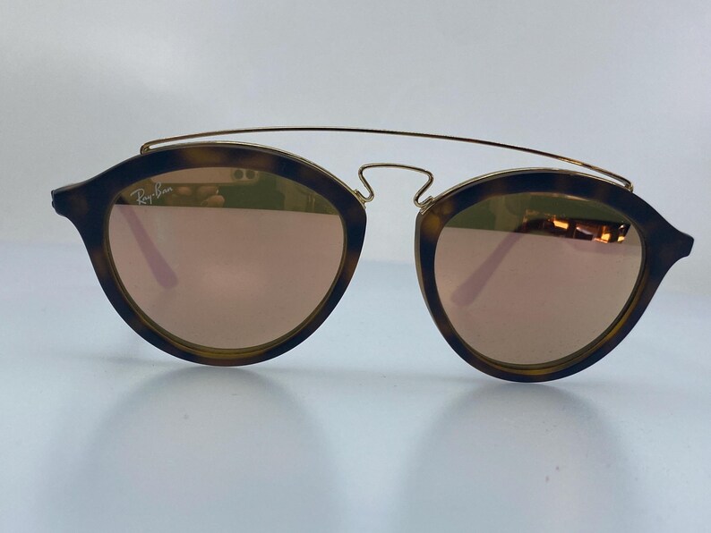 May include: Tortoise shell frame sunglasses with gold accents and mirrored lenses. The lenses are a rose gold color.