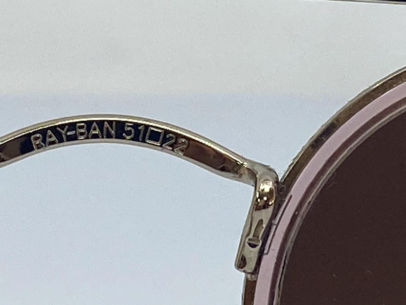 Puede incluir: Primer plano del brazo de metal plateado de unas gafas de sol redondas. El brazo est&aacute; grabado con el texto "RAY-BAN 51□22".