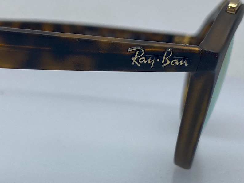 May include: Close-up of a pair of tortoiseshell Ray-Ban sunglasses. The sunglasses have a gold logo on the side.