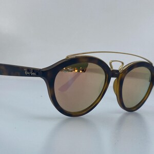 May include: Tortoise shell Ray-Ban sunglasses with gold accents and rose-colored lenses.