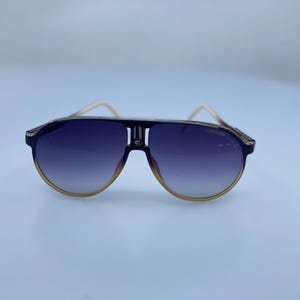 May include: A pair of aviator sunglasses with a dark brown frame and gradient gray lenses. The sunglasses have a white stripe across the bridge of the nose.