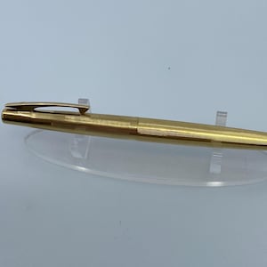 Puede incluir: Un bolígrafo de fuente de tono dorado con un barril texturizado y un clip en la parte superior.