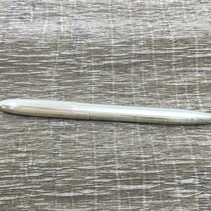 Puede incluir: Un bolígrafo plateado con un extremo redondeado y un acabado liso y pulido.