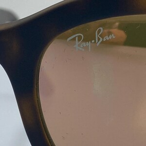 May include: Close-up of a pair of tortoiseshell Ray-Ban sunglasses with a pink lens. The Ray-Ban logo is visible on the right lens.