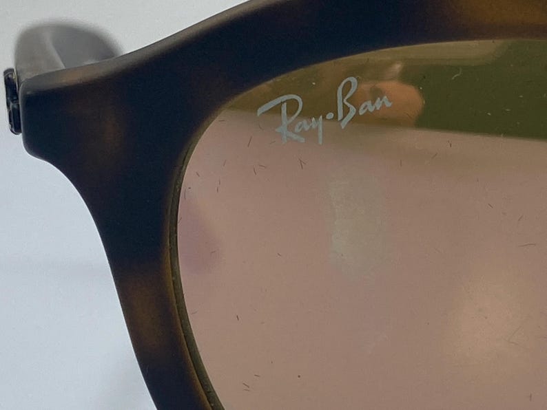 May include: Close-up of a pair of tortoiseshell Ray-Ban sunglasses with a pink lens. The Ray-Ban logo is visible on the right lens.