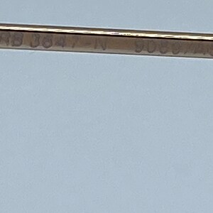Puede incluir: Primer plano de un marco de metal dorado con el texto "RB 3847-IN 9088/45" grabado en &eacute;l.