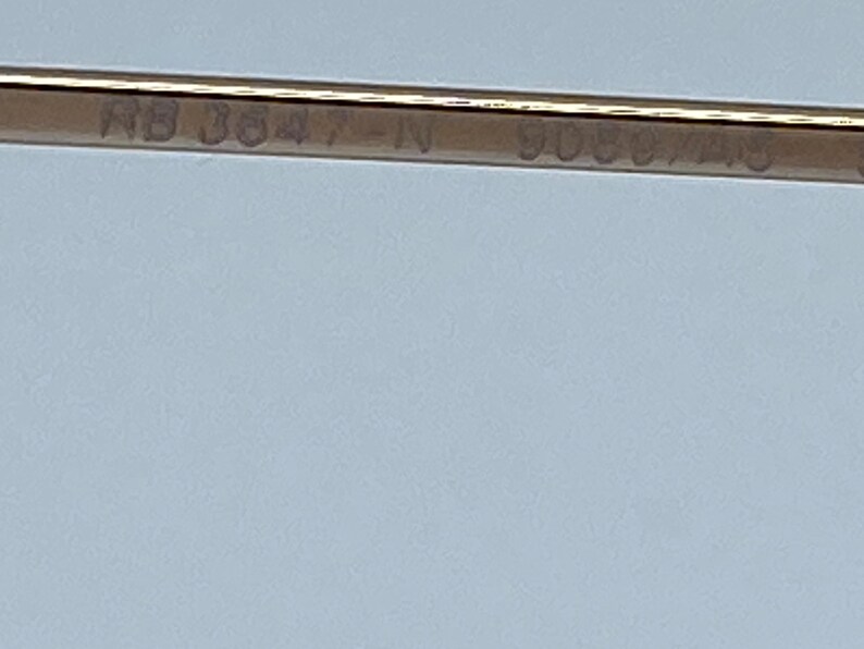 Puede incluir: Primer plano de un marco de metal dorado con el texto "RB 3847-IN 9088/45" grabado en &eacute;l.