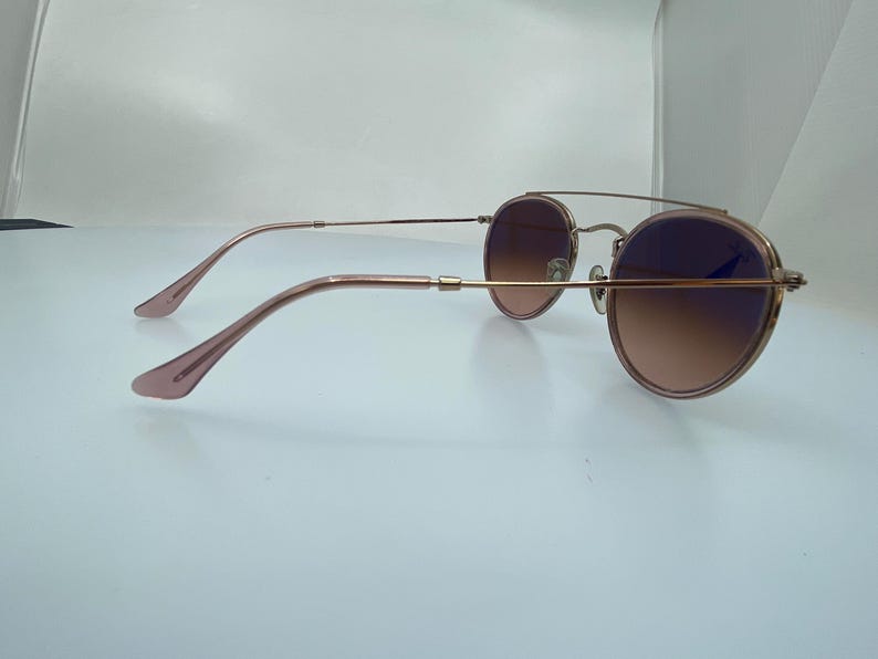 Puede incluir: Gafas de sol redondas de oro rosa con lentes marrones degradados. Las gafas tienen un fino marco de metal y se muestran de lado.