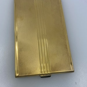 May include: A gold-colored metal compact with a textured surface and a hinged lid.