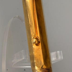May include: A gold-colored fountain pen cap with a smooth, reflective surface and a rounded clip attachment. The metal surface features a small, stamped hallmark reading 925, indicating sterling silver composition beneath the gold-toned finish.