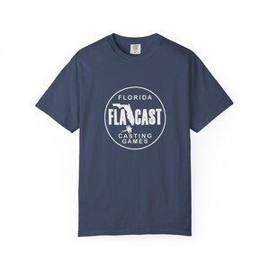May include: Navy blue t-shirt with a white circular graphic. The graphic features the word "FLA CAST" inside a circle, with "FLORIDA" above and "CASTING GAMES" below. A stylized image of Florida is in the center of the graphic.