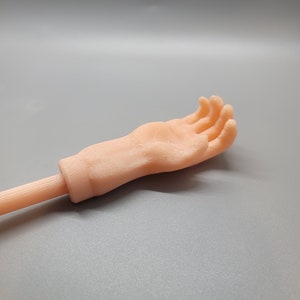 May include: A 3D printed hand with a flesh-toned color, attached to a stick. The hand is open and facing upwards.
