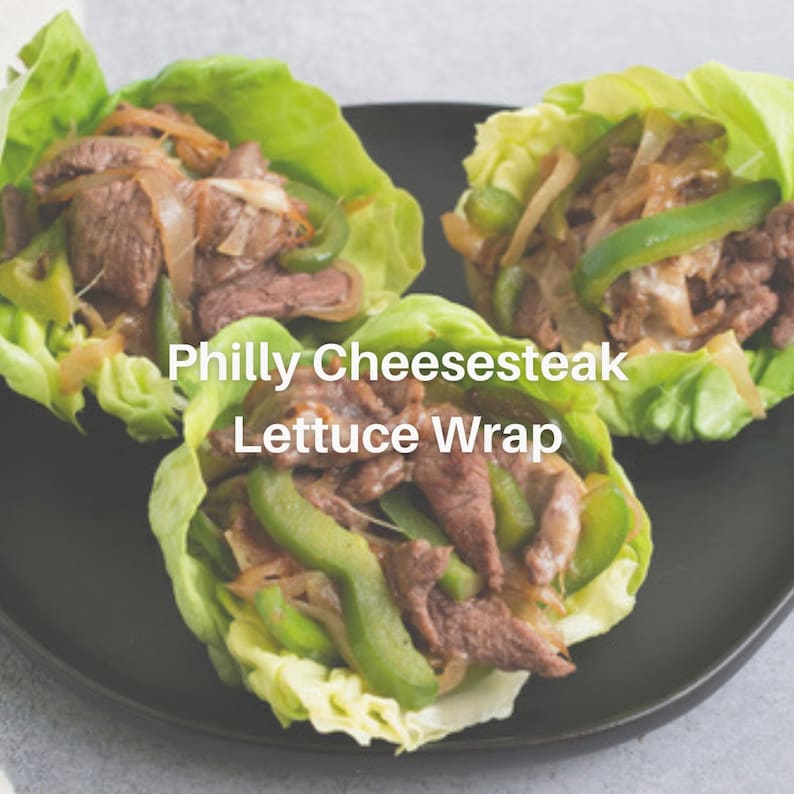 Puede incluir: Tres wraps de lechuga rellenos de filete de ternera cortado fino, pimientos verdes y cebollas. Los wraps est&aacute;n en un plato negro y el texto "Philly Cheesesteak Lettuce Wrap" est&aacute; escrito debajo de los wraps.