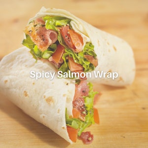 Puede incluir: Un wrap de tortilla blanco relleno de lechuga, tomate, tocino y salm&oacute;n. El wrap est&aacute; doblado por la mitad y tiene la etiqueta "Spicy Salmon Wrap".