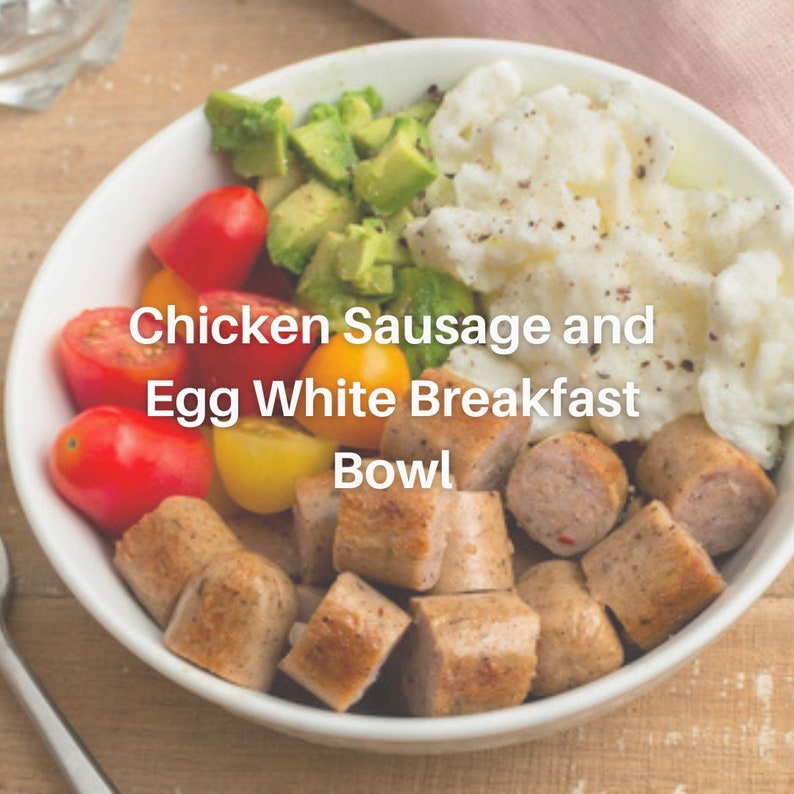 Puede incluir: Un bol blanco lleno de una comida de desayuno de salchicha de pollo, claras de huevo, aguacate y tomates cherry. El bol est&aacute; sobre una superficie de madera. El texto "Chicken Sausage and Egg White Breakfast Bowl" est&aacute; escrito en la imagen.