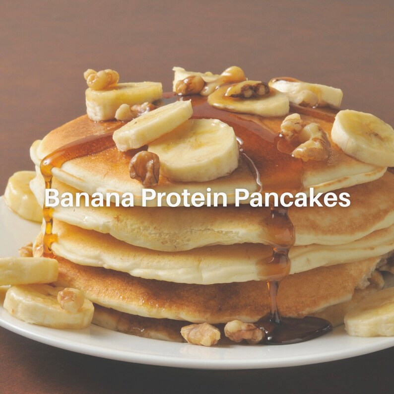 Puede incluir: Una pila de cuatro panqueques dorados, cubiertos con rodajas de pl&aacute;tano, nueces picadas y un chorrito de jarabe de arce. Los panqueques est&aacute;n en un plato blanco con un fondo marr&oacute;n. El texto "Banana Protein Pancakes" est&aacute; superpuesto en la imagen.