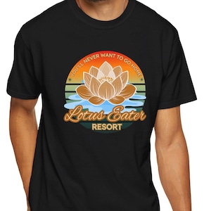 May include: Black t-shirt featuring a circular graphic with a lotus flower design. The graphic includes the text "YOU'LL NEVER WANT TO GO HOME" and "Lotus Eater RESORT" in a retro style. The design incorporates orange, yellow, and blue hues.