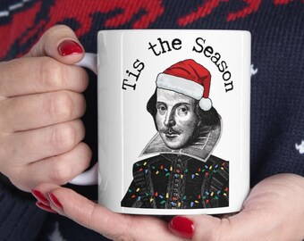 Könnte beinhalten: Weiße Keramiktasse mit einer Schwarzweißillustration von William Shakespeare, der einen Weihnachtsmann-Hut und eine Lichterkette trägt. Der Text "Tis the Season" ist auf die Tasse gedruckt.