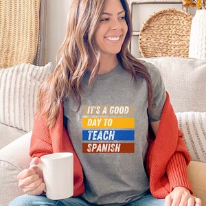 May include: A gray t-shirt with the text "It's a good day to teach Spanish" in colorful block letters.