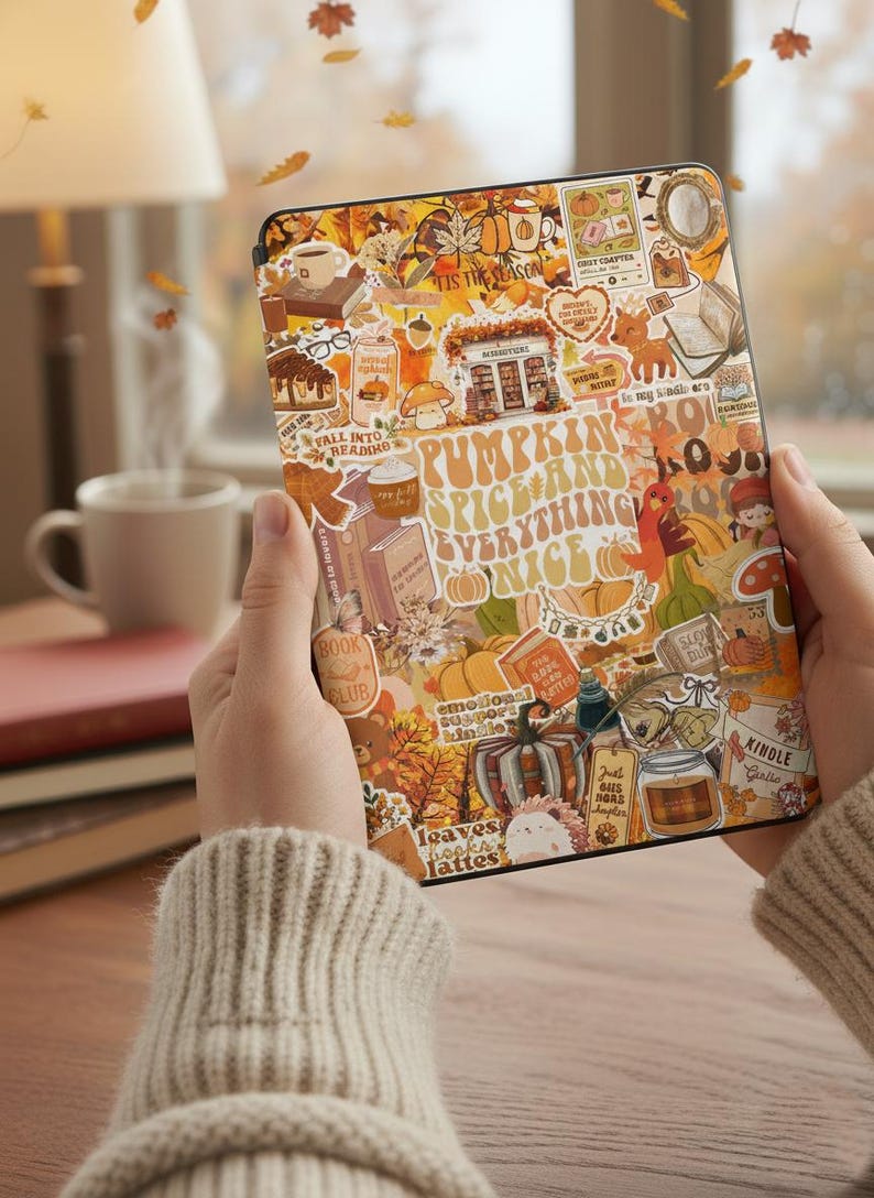 May include: A Kindle e-reader with a fall-themed sticker design. The stickers feature pumpkins, books, coffee, and the text "Pumpkin Spice and Everything Nice." The e-reader is held in front of a blurred background with falling leaves.
