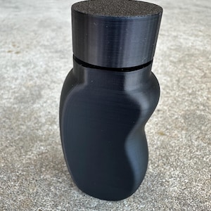 Puede incluir: Una botella de plástico negra con una tapa texturizada. La botella está vacía y tiene una forma redonda y lisa.